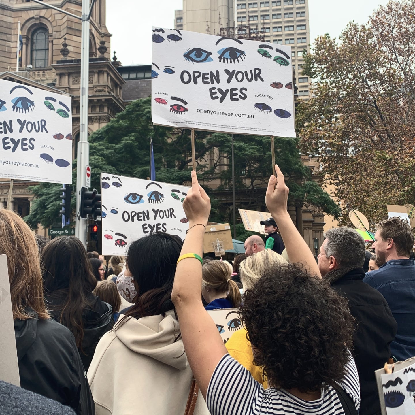 Masked Australian Ethical employees attending a 2021 Sydney Climate Rally and holding up Open Your Eyes signs